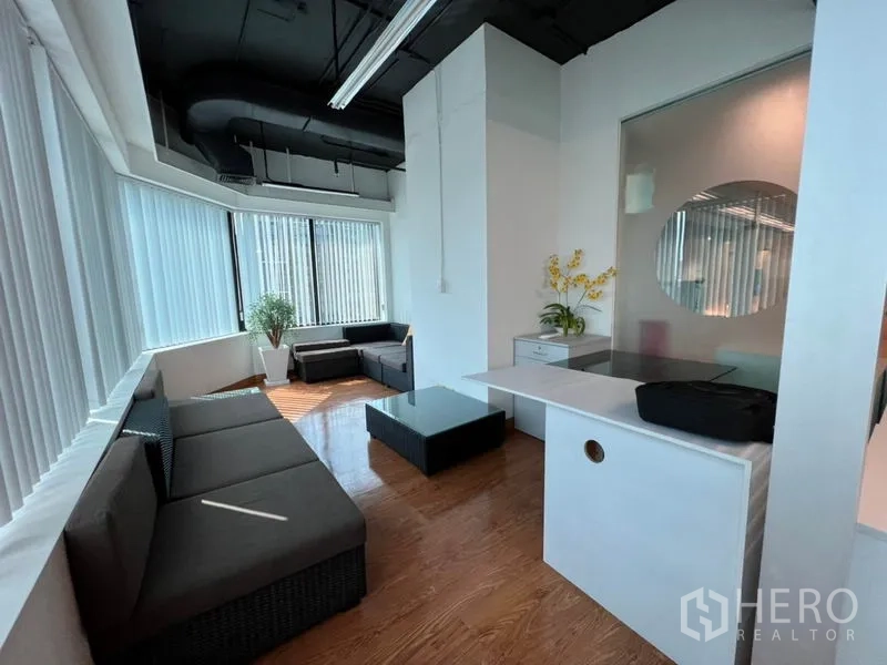 Office Space for rent in Khlong Toei, Bangkok - Bright lounge area with sectional sofas, a coffee table and corner windows with blinds.