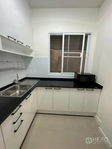 Townhouse for rent in Chom Thong, Bangkok - L-shaped white kitchen cabinetry with black countertops and a window.