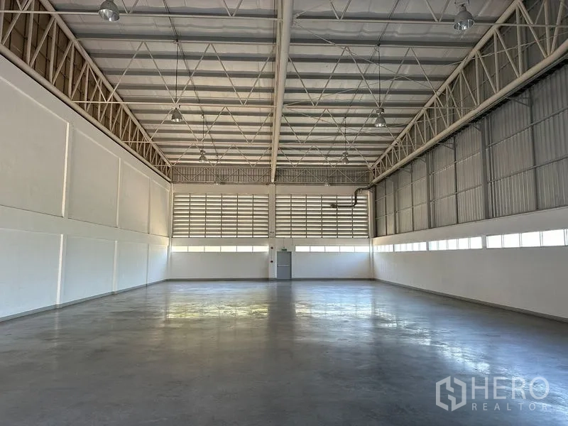 Factory for rent in Bang Bo, Samut Prakan - Wide warehouse interior with high ceiling, louvered windows and a loading door at the far end.
