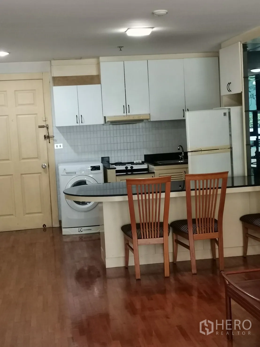 คอนโด ให้เช่าในPathum Wan, Bangkok - ครัวขนาดกะทัดรัดตู้สีขาว เคาน์เตอร์บาร์ ตู้เย็น และเครื่องซักผ้าในห้อง บนพื้นไม้