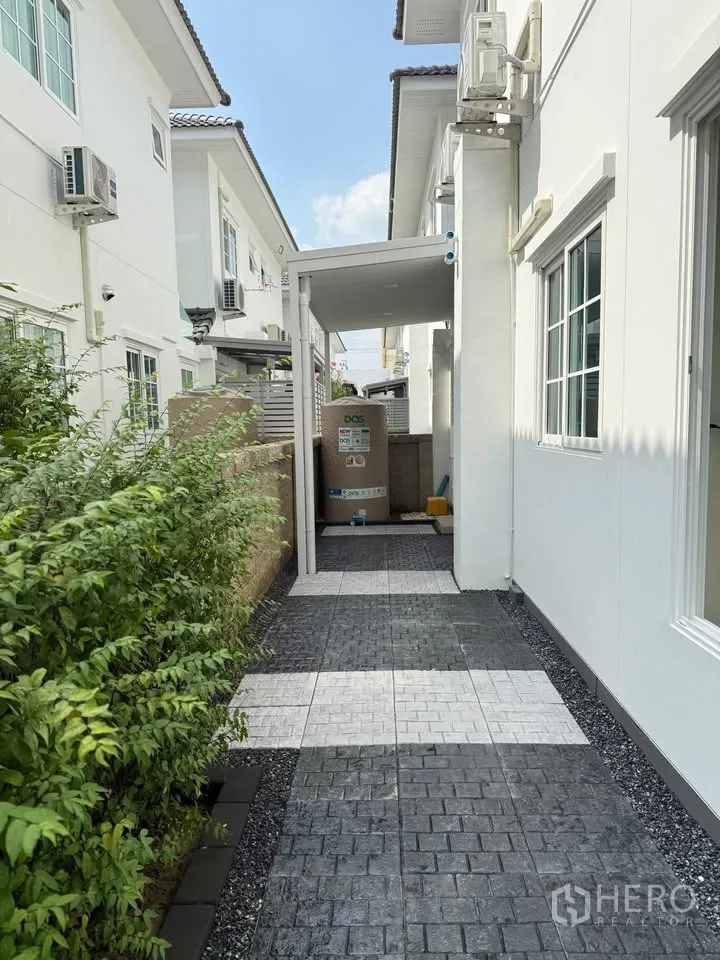 บ้านแฝด for rent in Mueang Samut Prakan, Samut Prakan - ทางเดินข้างบ้านปูพื้นลายสลับ มีพุ่มไม้และพื้นที่อเนกประสงค์มีหลังคา
