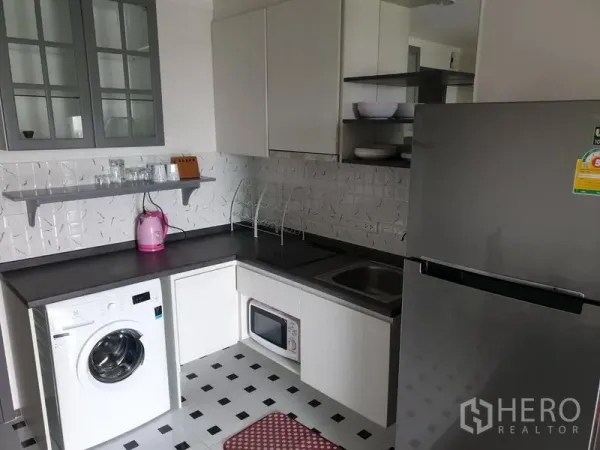 Condominium for rent in Watthana, Bangkok - Compact L-shaped kitchen with cabinets, fridge, sink, microwave, and washing machine.
