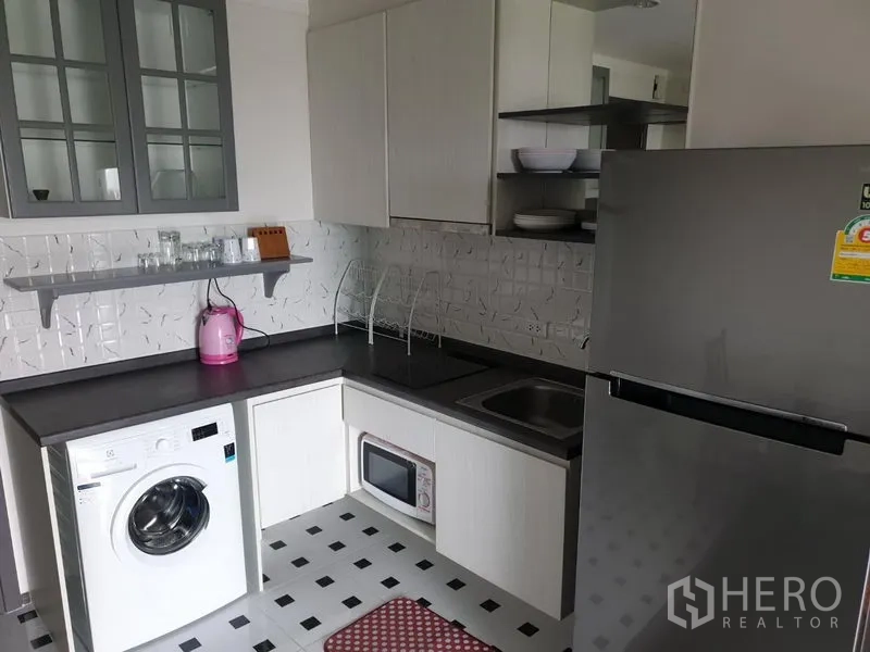 Condominium for rent in Watthana, Bangkok - Compact L-shaped kitchen with cabinets, fridge, sink, microwave, and washing machine.