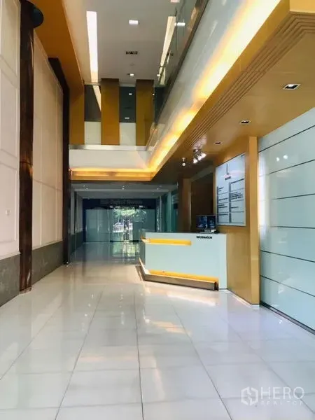 สำนักงาน ให้เช่าในRatchathewi, Bangkok - ล็อบบี้เพดานสูงพร้อมเคาน์เตอร์ต้อนรับ พื้นกระเบื้องเงา และไฟโทนอุ่นในอาคารสำนักงานสมัยใหม่