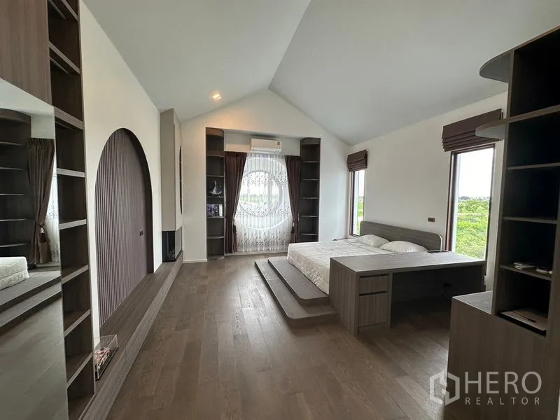 Detached House for sale in Sai Noi, Nonthaburi - Wide master suite with step-up bed, shelving and a round niche feature over wood floors.