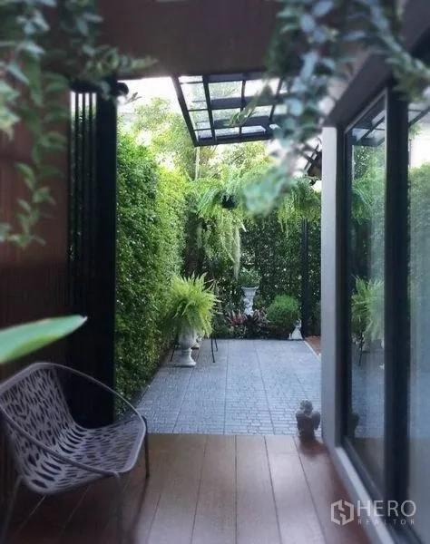 Detached House for sale in Nonthaburi - Side patio with glass sliding doors, canopy roof and hedge-lined walkway.