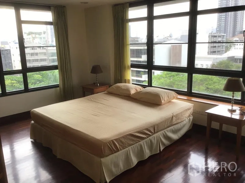 คอนโด ให้เช่าในWatthana, Bangkok - ห้องนอนมุมกระจกบานใหญ่ เห็นวิวเมืองและต้นไม้ พร้อมเตียงควีนและโต๊ะข้างเตียง