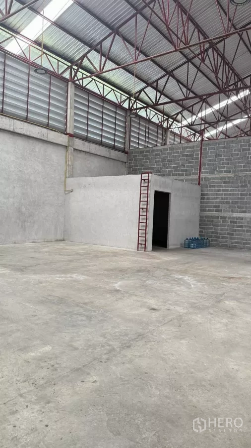 Warehouse for rent in Min Buri, Bangkok - Corner of warehouse with small built-in office room and ladder beside open concrete floor.
