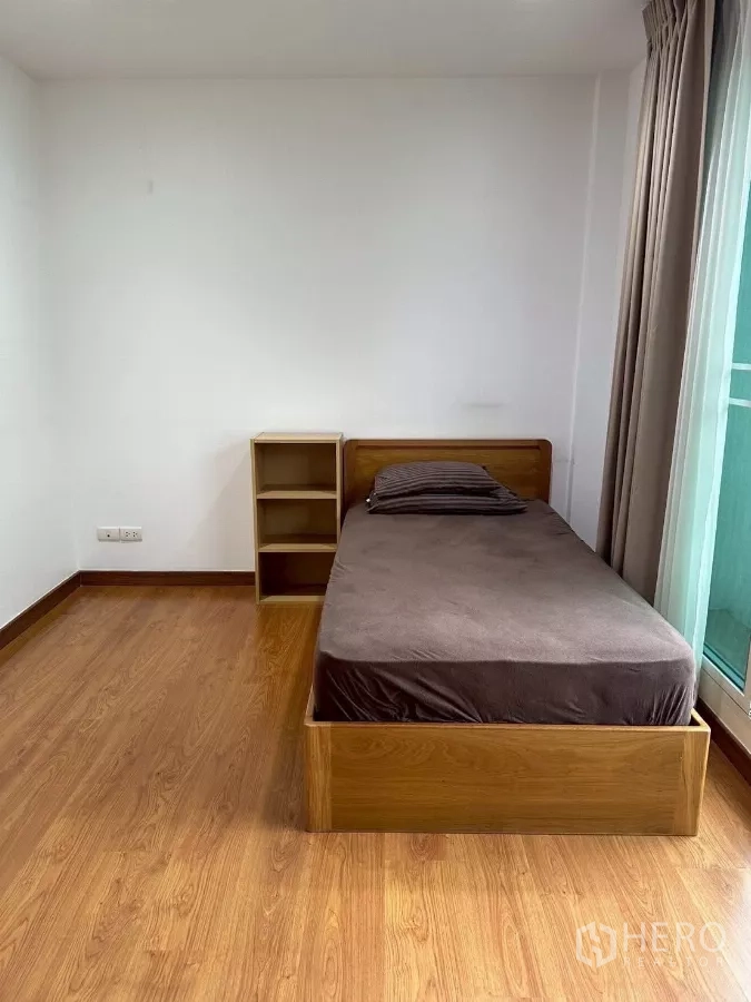 Townhouse for rent in Chom Thong, Bangkok - Bedroom with single bed beside balcony door and small shelving.
