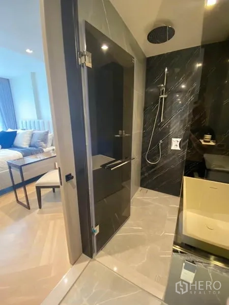 Condominium for rent in Watthana, Bangkok - Hotel-style bathroom with glass shower, black marble wall and rainfall showerhead, bedroom visible beyond.