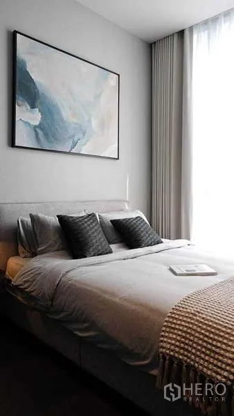 Condominium for rent or sale in Watthana, Bangkok - Cozy bedroom with artwork above the bed and sheer curtains filtering natural light.