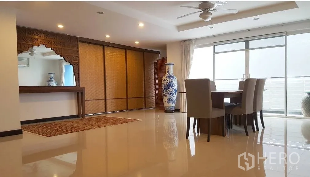 Condominium for rent in Watthana, Bangkok - Bright living and dining area of a Watthana Bangkok condo with sliding glass doors to the balcony, ceiling fan, and carved wooden feature.