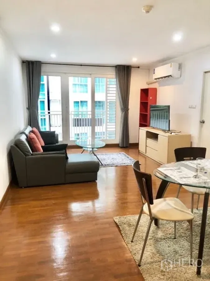 Condominium for rent or sale in Watthana, Bangkok - Bright open-plan living and dining area with gray sofa, glass coffee table, TV console, and balcony doors in a Watthana Bangkok condo.
