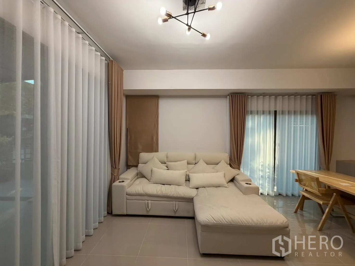 Townhouse for rent in Bang Phli, Samut Prakan - Bright lounge with L-shaped sofa beside two sliding glass doors and full-length curtains.