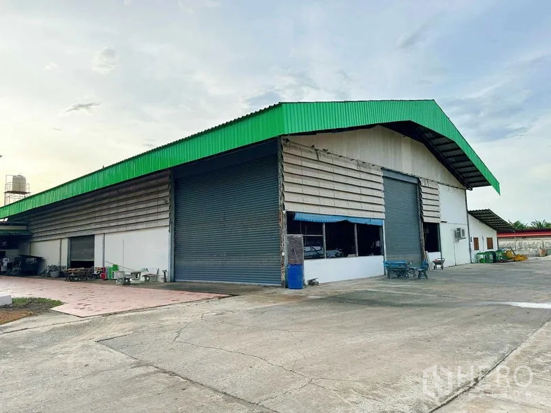 Warehouse for rent in Sai Noi, Nonthaburi - Side angle of the warehouse showing multiple shutter doors and a loading area on the concrete yard.