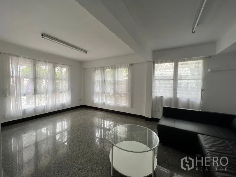 Detached House for rent in Saphan Sung, Bangkok - Bright family room with L-shaped sofa, round glass coffee table and large windows.