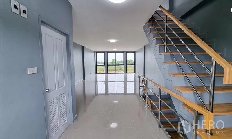 Shophouse for sale in Lam Luk Ka, Pathum Thani - Hallway beside the staircase leading toward the glazed frontage and views.