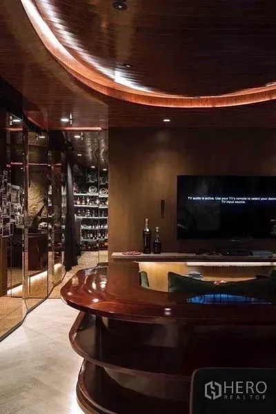 公寓 出租在Watthana, Bangkok - 客厅采用弧形木质天花、壁挂电视与亮面内置吧台及玻璃展示柜