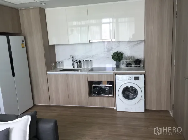 Condominium for sale in Bang Rak, Bangkok - Open-plan kitchen with white cabinets, marble backsplash, sink, washing machine and tall fridge in a Bang Rak condo.