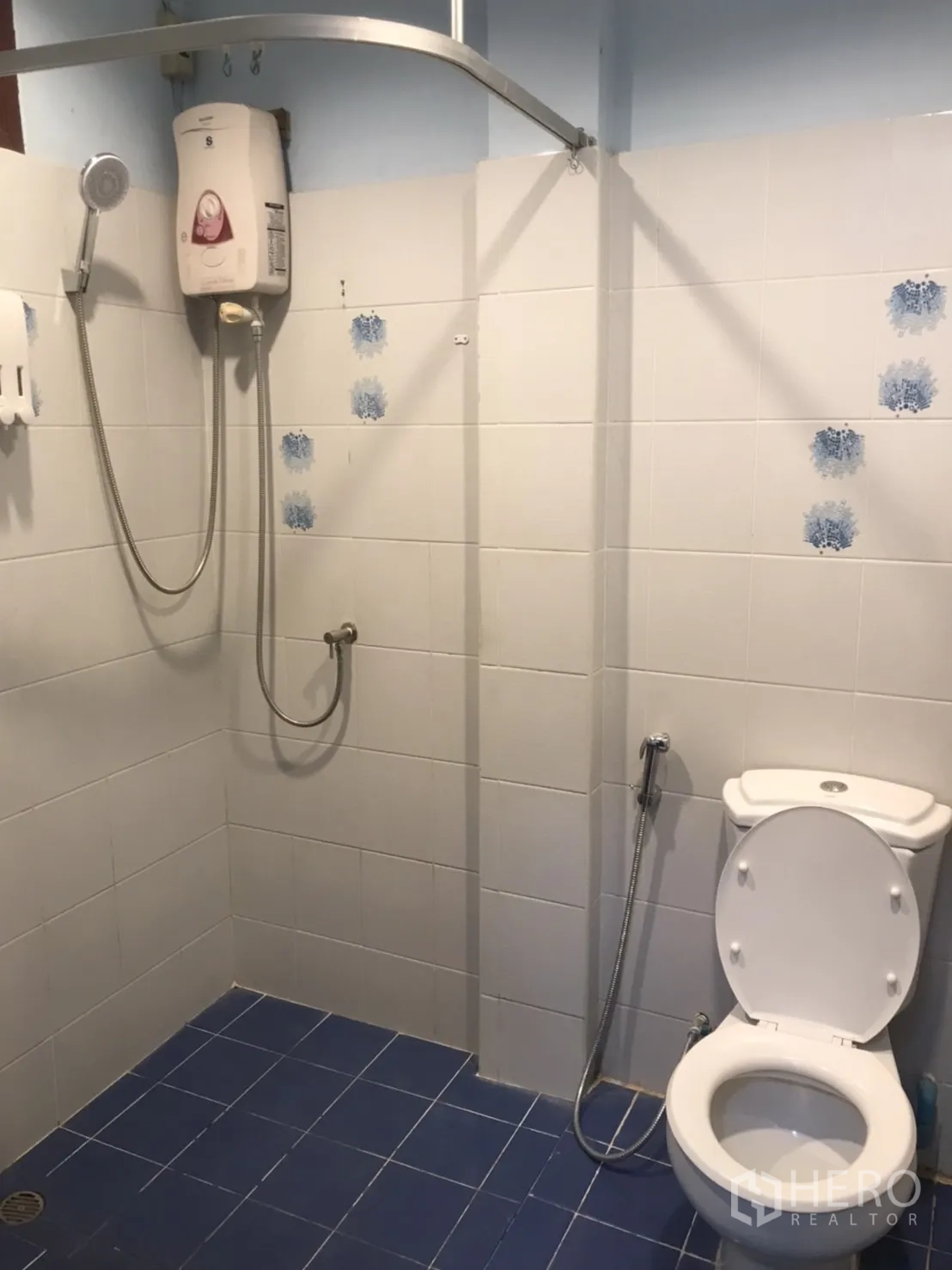 Home Office for rent in Khlong Toei, Bangkok - Bathroom with shower, water heater, handheld bidet spray, and toilet on blue tiled floor.