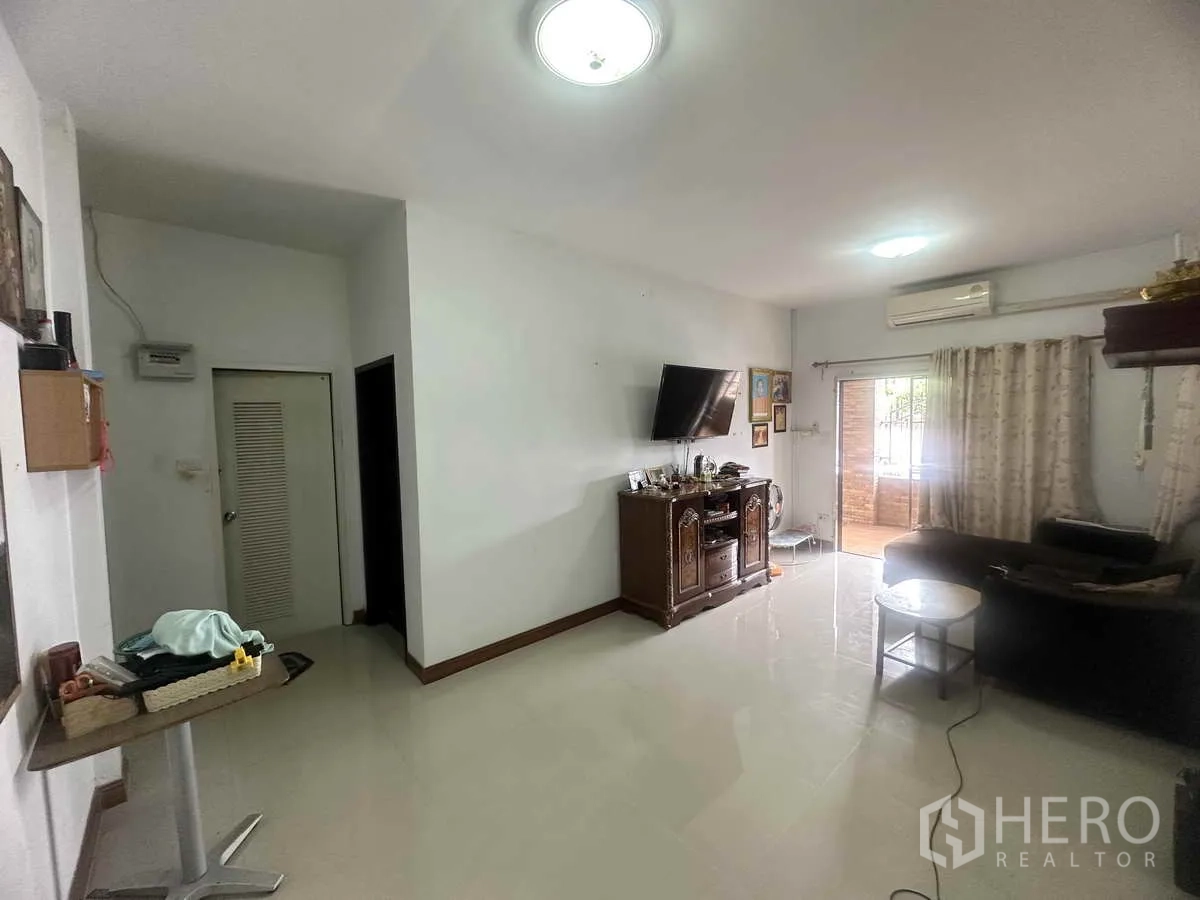 独立式住宅 出售在Pathum Thani - 明亮客厅，瓷砖地面，墙挂电视，通向露台的推拉门。