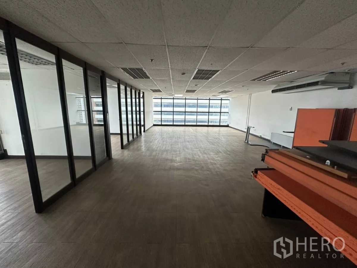 Office Space for rent in Watthana, Bangkok - Deep office bay lined with glass partitions on one side, large windows ahead, and wood-style flooring throughout.