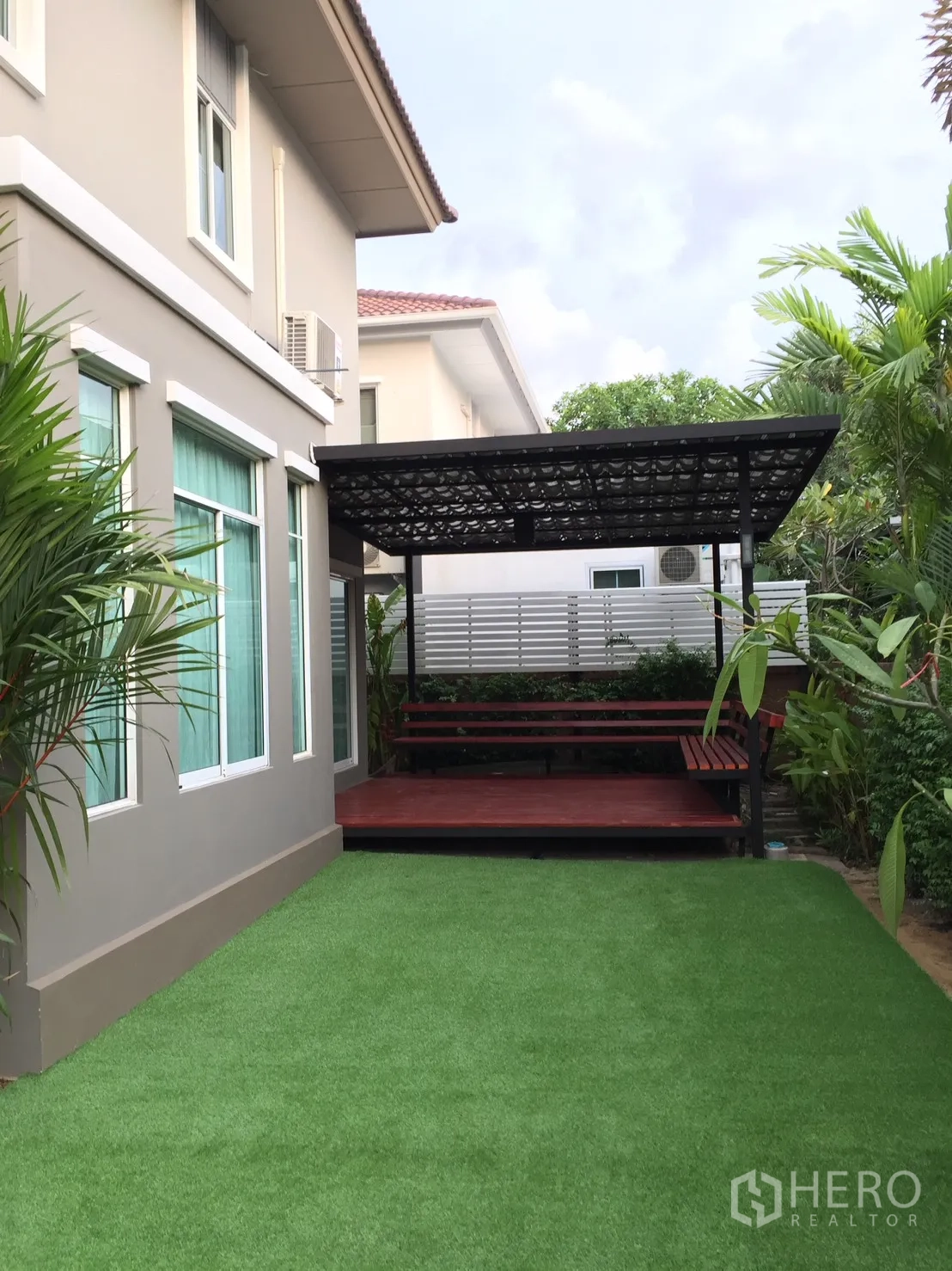 Detached House for rent in Pathum Thani - Backyard with synthetic lawn and a covered wooden deck beside the house.