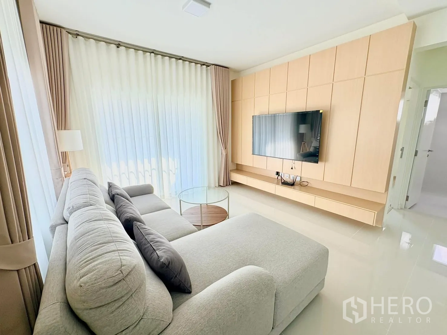 独立式住宅 for rent in Bang Phli, Samut Prakan - 客厅内L形沙发对着电视，纱帘与圆形玻璃茶几点缀其间。
