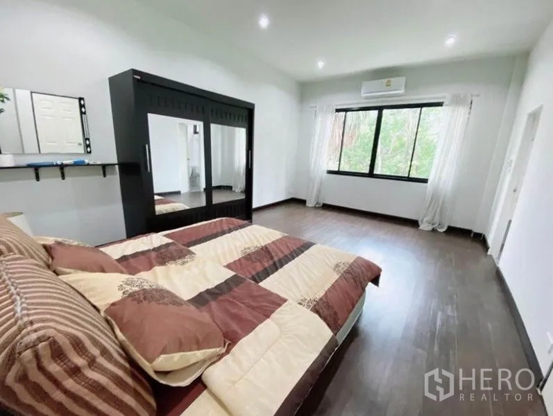 Townhouse for rent in Wang Thonglang, Bangkok - Large bedroom with wardrobe, air-conditioning, and wide window overlooking greenery.