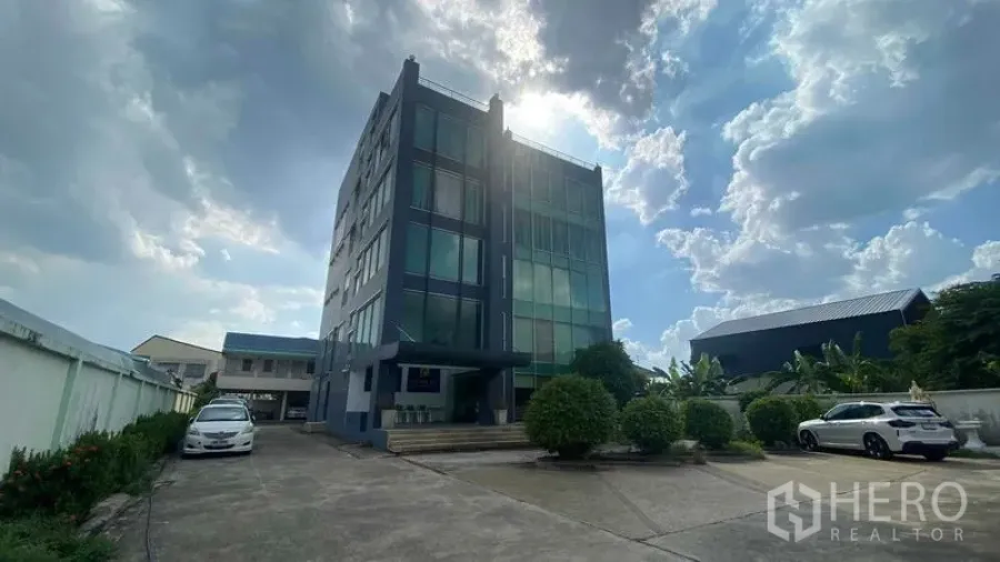 Office Space for sale in Bang Kapi, Bangkok - Exterior view of the glass-front office building with surface parking and greenery.