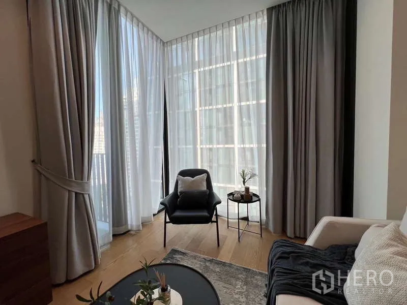 คอนโด ให้เช่าในPathum Wan, Bangkok - มุมนั่งเล่นสว่างด้วยเก้าอี้เอนหลัง ข้างผ้าม่านโปร่งและกระจกสูง มองเห็นวิวเมือง