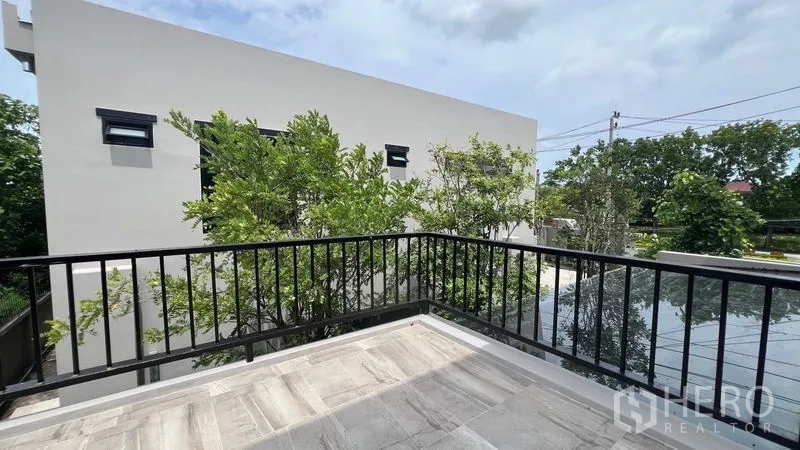 บ้าน ให้เช่าในLat Krabang, Bangkok - ระเบียงชั้นสองราวเหล็ก มองเห็นต้นไม้และบ้านสมัยใหม่รอบข้าง
