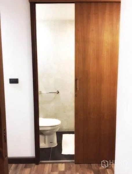 Townhouse for rent in Bang Rak, Bangkok - Compact bathroom visible through a sliding wooden door with minimalist finishes.