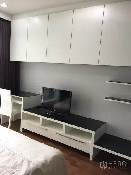 Condominium for rent in Pathum Wan, Bangkok - Bedroom wall with white built-in cabinets, study desk and TV console.
