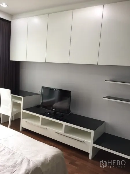 Condominium for rent in Pathum Wan, Bangkok - Bedroom wall with white built-in cabinets, study desk and TV console.