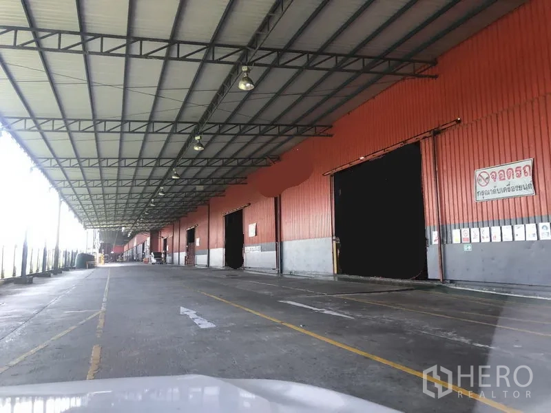 Warehouse for sale in Wang Noi, Phra Nakhon Si Ayutthaya - Long covered loading dock on a red warehouse facade with multiple roller doors and truck lanes.