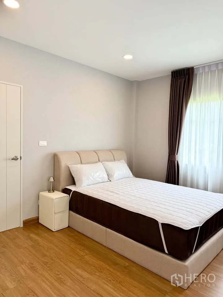 Detached House for rent in Bang Phli, Samut Prakan - Cozy bedroom with upholstered bed, bedside table, and curtained window.