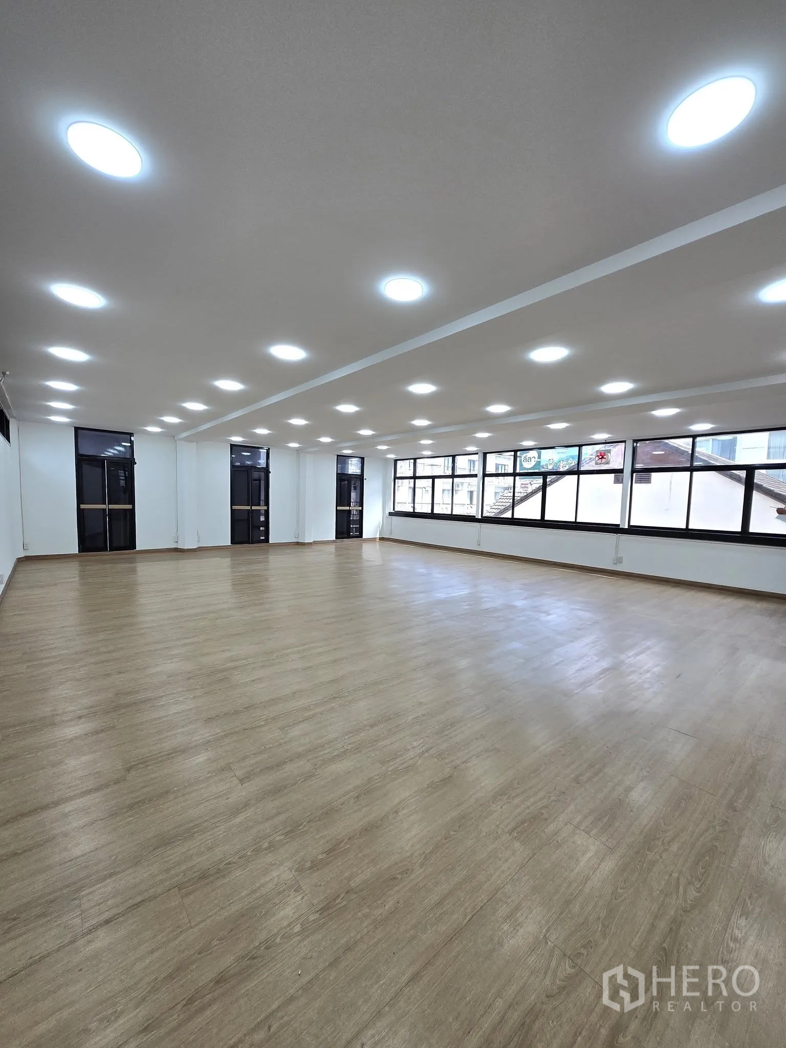 Office Space for rent in Khlong Toei, Bangkok - Large open-plan office with wood-look flooring, many ceiling lights, and wide windows.