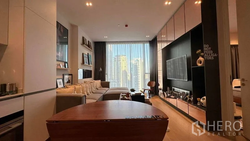 Condominium for sale - Modern Thonglor condo living room with L‑shaped sofa, TV wall and floor‑to‑ceiling window with city view.
