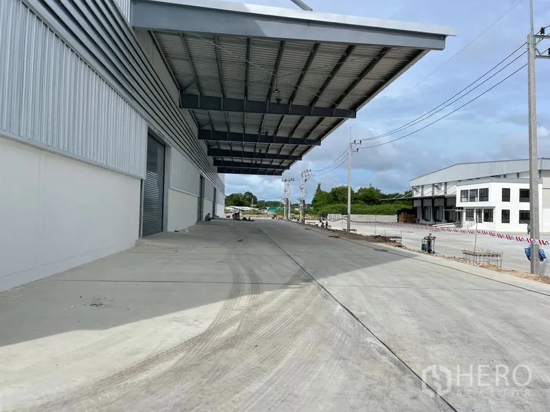 工厂 出租在Mueang Rayong, Rayong - 带雨棚的装卸月台与侧向车道，旁有电线杆和工业建筑。