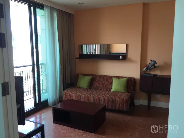 คอนโด ให้เช่าในKhlong Toei, Bangkok - ห้องนั่งเล่นสว่าง โซฟาลายทาง โต๊ะกลาง ผนังสีพีช และประตูกระจกออกสู่ระเบียง