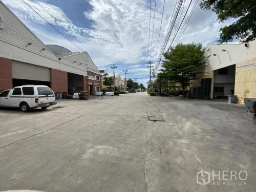 货栈 出租在Samut Sakhon - 宽阔混凝土街道，两侧为仓库并有架空电缆。