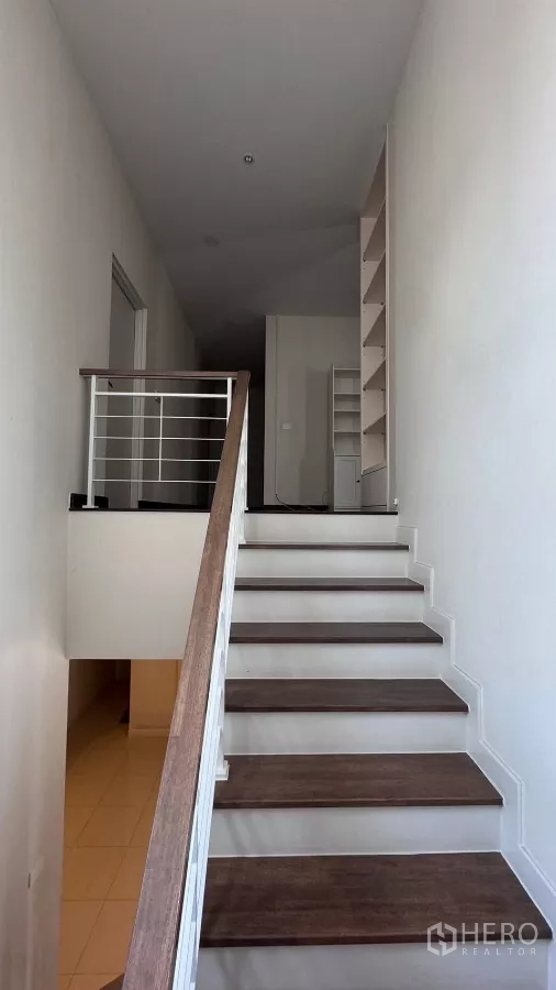 บ้าน ให้เช่าหรือขายในSaphan Sung, Bangkok - บันไดขั้นไม้ราวสีขาวสู่ชั้นบน พร้อมชั้นวางของบริเวณโถงทางเดิน.