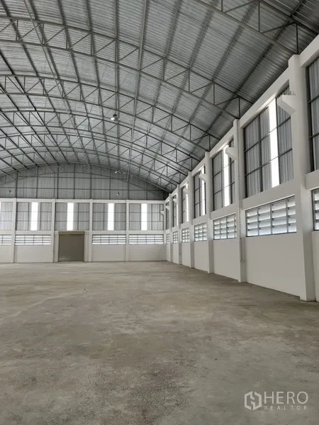 Factory for rent or sale in Bang Bo, Samut Prakan - Long interior view of a bright factory hall with rows of windows and curved steel truss roof.
