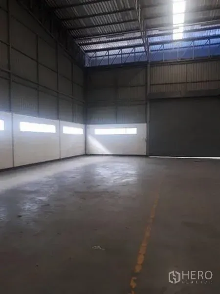 Warehouse for rent in Si Racha, Chon Buri - Empty warehouse bay with high ceiling, concrete floor, and daylight windows along the walls.
