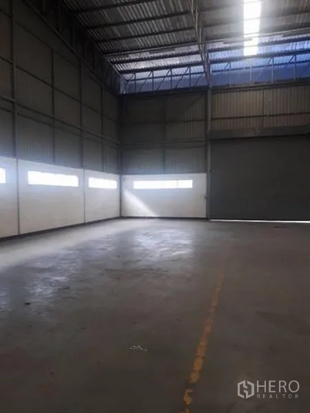 Warehouse for rent in Si Racha, Chon Buri - Empty warehouse bay with high ceiling, concrete floor, and daylight windows along the walls.