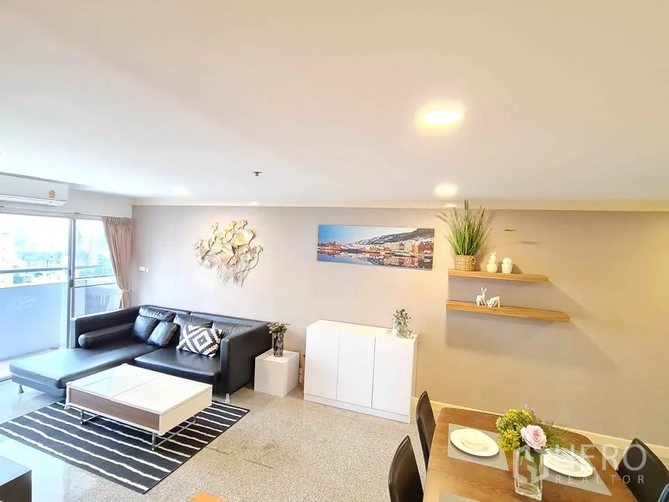 Condominium for rent in Khlong Toei, Bangkok - Bright lounge with sofa, wall shelves and artwork near balcony doors.