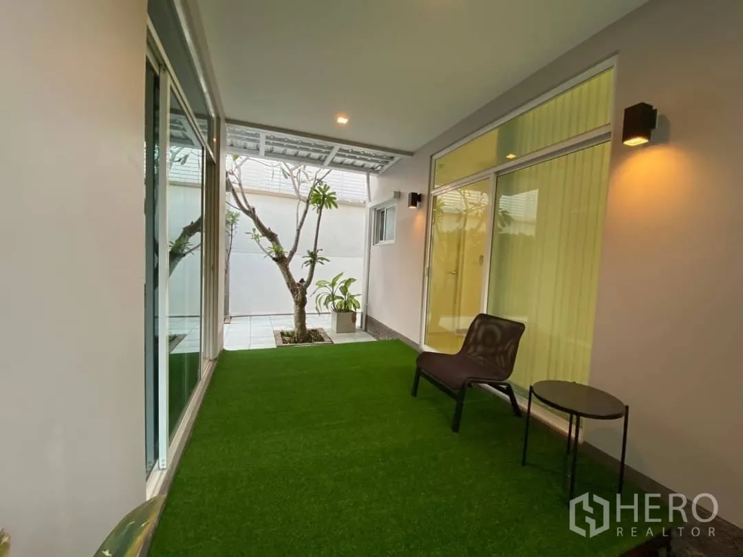 独立式住宅 出租或出售在Prawet, Bangkok - 覆盖式露台，铺人造草坪，推拉玻璃门与壁灯连接室内空间。