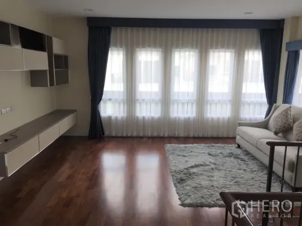 Detached House for rent or sale in Saphan Sung, Bangkok - Bright living room with floor-to-ceiling windows, sheer curtains and wooden flooring.