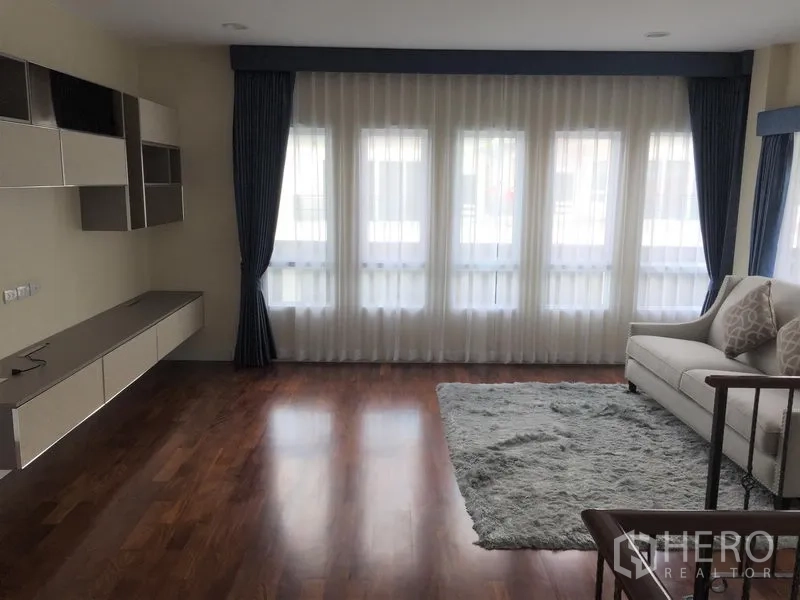 Detached House for rent or sale in Saphan Sung, Bangkok - Bright living room with floor-to-ceiling windows, sheer curtains and wooden flooring.